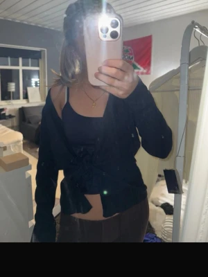 Svart croppad knytblus - Snygg svart croppad blus med knyt framtill och långa ärmar. Perfekt att styla med ett linne under för en trendig lager-på-lager-look. Enkel och stilren design som passar till många outfits.