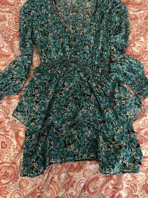 Blommig kortklänning från Zara - Supersöt kortklänning från Zara med blått och grönt blommönster. Klänningen har v-ringning, långa ärmar och markerad midja. Tunt, lätt material som passar perfekt till varmare dagar. Snygg och trendig modell med volangdetaljer.