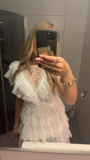 Vit spetsklänning med volanger - Använd en endaste gång och ser ut som ny. Nypris 899kr!💕             Säljer en vit kort klänning med flera lager volanger och spetsdetaljer. Klänningen har v-ringad hals och är ärmlös, perfekt till studenten eller konfirmationen. Materialet är i spets. 😇