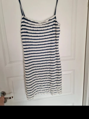Randig kortklänning med smala axelband - Säljer en vit och marinblå randig kortklänning med smala axelband. Klänningen har en enkel och rak form, perfekt för varma dagar. Materialet känns mjukt och lätt. Passar dig som gillar en avslappnad och somrig stil. Har skön underklänning.