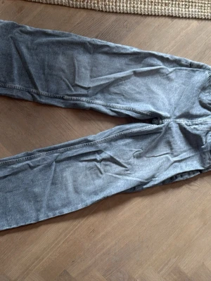 Grå wide leg jeans från H&M - Wide leg jeans från H&M i grått denim med hög midja och justerbar midja. Snygga och trendiga med avslappnad passform, perfekta för dig som gillar en cool och bekväm stil.