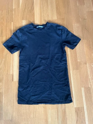 Svart basic t-shirt i bomull - En enkel svart t-shirt i mjuk bomull med rund hals och korta ärmar. Perfekt till jeans eller shorts för en clean och avslappnad look. Klassisk passform utan tryck eller detaljer.
