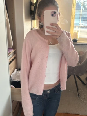 Ljusrosa mysig kofta med knappar - Säljer en ljusrosa kofta med rund hals och knäppning framtill. Koftan är mjuk och har långa ärmar, perfekt att slänga över en topp. Materialet ser ut att vara fluffigt och skönt, passar dig som gillar en chill och söt stil.