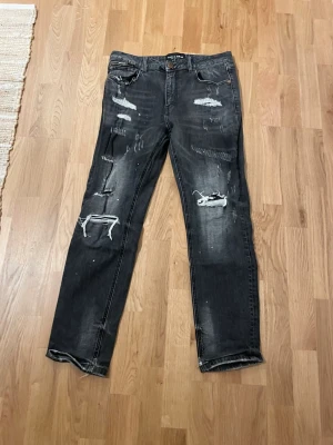 Svarta distressed jeans Supply & Demand - Säljer ett par svarta jeans från Supply & Demand med slitna detaljer och trasiga partier på benen. Jeansen har raka ben och klassisk femficksmodell. Perfekta för dig som gillar en edgy och trendig streetstyle-look.