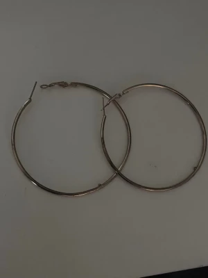 Stora guldfärgade hoops örhängen - Säljer ett par stora, tunna hoops örhängen i guldfärgad metall. Klassisk rund form som passar till många olika stilar. Perfekta för dig som gillar statement-smycken och vill ha något enkelt men ändå snyggt.