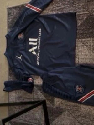 Mörkblå PSG träningsset från Puma - Säljer ett mörkblått träningsset från PSG och Puma med långärmad tröja och matchande byxor. Setet har vita och röda detaljer, PSG-logga och Puma-logga på bröstet samt texten 'Accor Live Limitless' på tröjan. Perfekt för fotbollsträning.