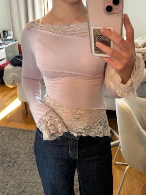 Ljusrosa långärmad topp med spets - Säljer en ljusrosa långärmad topp med transparent spetsdetaljer vid ärmslut, midja och halsringning. Toppen har en figurnära passform känns mjukt och stretchigt ❤️ lite sliten vid spetsdetaljerna 