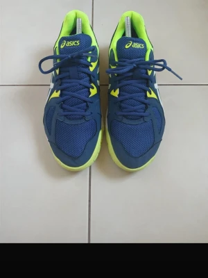 Blå och neongula Asics sneakers - Fräscha sneakers från Asics i blått och neongult med vita detaljer. Skorna har meshpaneler för extra ventilation, klassisk Asics-logga på sidan och en sportig siluett. Yttersulan är neongul och ger en cool kontrast till resten av skon.