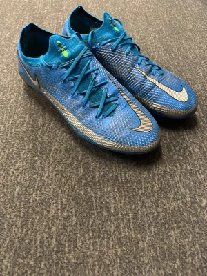 Nike phantom  - Säljer ett par blå Nike Mercurial fotbollsskor med silverdetaljer och klassisk låg profil. Skorna har snörning, mönstrad ovandel i syntetmaterial och dobbar för bra grepp på planen. Perfekta för dig som vill ha speed och kontroll på matchen.