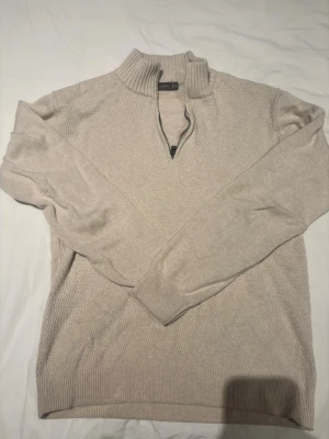 Beige stickad tröja med halv dragkedja - Snygg beige stickad tröja med halv dragkedja M men passar S bättre och hög krage. Tröjan har långa ärmar och ribbade muddar vid ärmslut och nederkant. Perfekt för lager på lager och enkel att matcha med olika outfits.