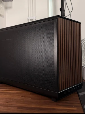 Stilren stationär dator med träpanel - Snygg stationär dator med svart metallchassi och frontpanel i trä. Kompakt och modern design med ventilerade sidor för bra luftflöde. Perfekt för gaming eller kreativa projekt, med flera USB-portar framtill och plats för kraftfulla komponenter.
