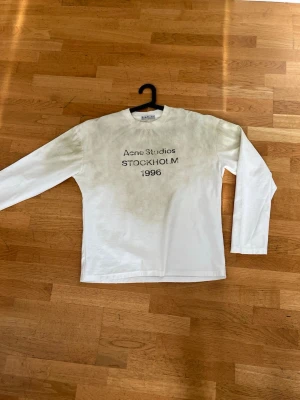 Vit långärmad topp Acne Studios - Vit långärmad topp från Acne Studios med tryck 'STOCKHOLM 1996' på bröstet. Klassisk rak passform och rund halsringning. Tillverkad i mjuk bomull, perfekt för en clean och enkel stil.
