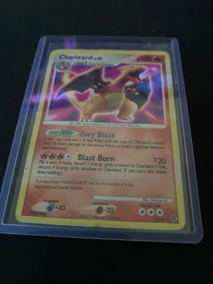 Charizard Pokémonkort 2007 - Säljer ett Charizard Pokémonkort från 2007 med starka färger och klassiskt motiv. Kortet är inplastat i ett skyddsfodral och har detaljer på både fram- och baksida. Perfekt för samlare eller Pokémonfans.