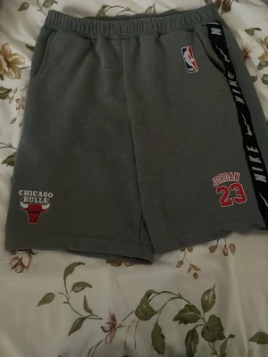Chicago Bulls grå shorts NBA - Snygg short  med Chicago Bulls-logga och NBA-märke . Perfekt för dig som älskar basket och vill visa vilket lag du hejar på. Shortsen har klassisk passform och är tillverkad i mjukt bomullsmaterial. Och längst ner till vänster så kan du se att det står Jordan 23