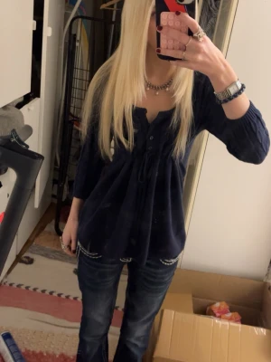 Mörkblå blus med knyt och knappar från hollister - Mysig mörkblå blus med trekvartsärm, knyt i midjan och knappar framtill. Blusen har en avslappnad passform och lätt v-ringad hals. Perfekt till jeans för en chill look.
