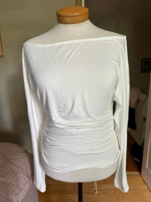 Vit topp från Lager 157 - Säljer en vit topp från Lager 157 i mjukt material. Toppen har lång ärm och smickrande rynkdetaljer vid midjan som ger en snygg siluett. Perfekt att styla med jeans eller kjol för en trendig look. I princip oanvänd.