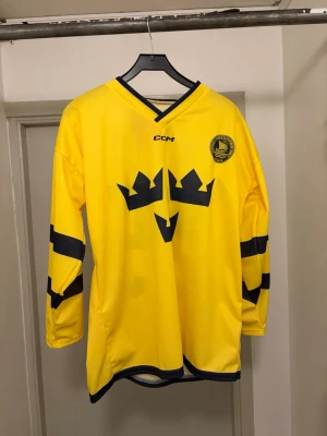 Gul Tre Kronor hockeytröja CCM - Säljer en Trekronor matchtröja från CCM från ett mycketlimiterat utskick från Nocco vilket innebär att du inte kan köpa tröjan någonstans . Tröjan har långa ärmar med svarta ränder, V-ringad krage och nummer 25 samt texten NOCCO på ryggen! Tröjan är aldrig använd och har kvar prislapp. Kan gå ner i pris vid snabb affär