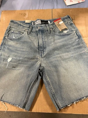 Ljusblå jeansshorts från Levi's - Snygga ljusblå jeansshorts från Levi's med råa kanter och slitna detaljer. Klassisk femficksmodell med knappgylf och bälteshällor. Perfekta för en avslappnad stil under varma dagar. Midjemåttet är ca:40cm (40+40) Alla lappar sitter kvar då de är oanvända. 