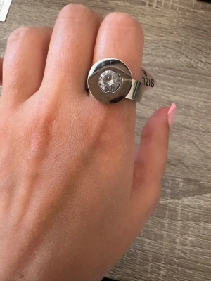 Stilren silverfärgad ring med sten från LenMer - Säljer en chunky ring i silverfärgad metall med en stor, rund klar sten i mitten. Ringen har en modern och minimalistisk design med bred ringband och polerad finish. Perfekt för dig som gillar statement-smycken och vill sticka ut. Ringen är i storlek 8 och helt oanvänd! OBS: FRAKTAR INOM 24H!🩷