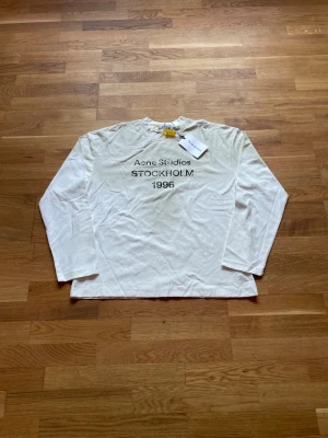 Acne Studios Longsleeve - Säljer en as fet Acne Studios Longsleeve med det klassiska "Acne Studios STOCKHOLM 1996" trycket på bröstet. Tröjans vita färg samt att den är i Longsleeve-varianten gör att den sticker ut i mangden. Storlek: Small men passar mer som medium. Mått- Längd: 69 cm. Axel till axel: 57.5 cm. Armhåla till armhåla: 57.5 cm. Helt ny! Skickas inom 24 timmar. Skriv vid funderingar!