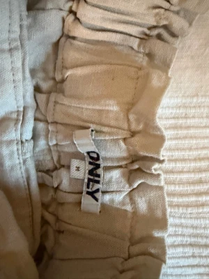 Beige shorts från ONLY med resår - Säljer ett par ljusbeige shorts från ONLY med bred resår i midjan. De har en avslappnad passform och är tillverkade i mjukt bomullstyg, perfekta för varma dagar. Passar dig som gillar enkel och bekväm stil.