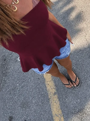 MISSÄY peplum tubtopp - Säljer en vinröd tubtopp med peplumskärning. Toppen är axelbandslös och har en snygg, utsvängd nederdel som ger en feminin siluett. Perfekt att styla med jeans eller kjol för en trendig look.