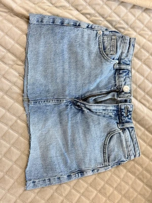 Ljusblå jeanskjol från VMD - Trendig ljusblå jeanskjol från VMD med rå kant nertill och klassisk femficksdesign. Kjolen har dragkedja och knapp framtill samt två stora bakfickor. Tillverkad i denim med en avslappnad och cool vibe.