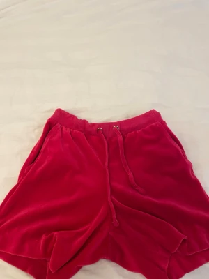 Rosa velourshorts med snörning - Mysiga rosa shorts i mjuk velour med bred resår i midjan och snörning framtill. Shortsen har sidofickor och en relaxed passform, perfekta för chill dagar eller sommarhäng.