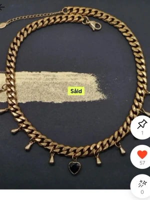 Maria Nilsdotter liknande  halsband med hjärta - Säljer ett halsband i guldfärgad metall med flera små droppformade hängen och ett svart hjärthänge i mitten. Kedjan är bred och har justerbar längd med karbinlås. Perfekt för dig som gillar statement-smycken och trendiga detaljer.