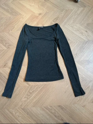 Mörkgrå långärmad topp H&M Divided - Mörkgrå långärmad topp från H&M Divided med rund halsringning. Modellen är slim fit och har en enkel, stilren design som passar till det mesta. Tillverkad i mjukt material som känns skönt mot huden. Den blir lite genomskinlig på. 