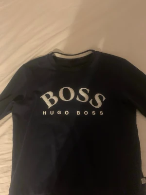Mörkblå sweatshirt från Hugo Boss - Snygg mörkblå sweatshirt från Hugo Boss med stort vitt BOSS-tryck på bröstet. Tröjan har rund halsringning och långa ärmar. Perfekt för en avslappnad och trendig look.