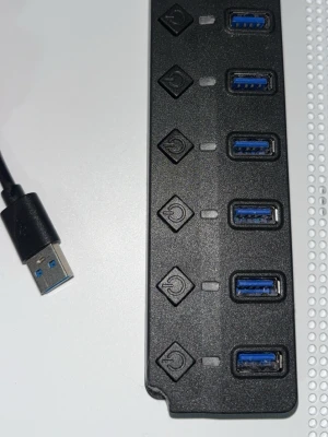 USB-hubb med individuella strömbrytare - En svart USB-hubb med fem USB 3.0-portar och individuella strömbrytare för varje port. Perfekt för att koppla flera USB-enheter till datorn samtidigt. Hubben har en rektangulär form och ansluts via en USB-kabel.