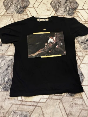Svart Off-White t-shirt med tryck - Svart t-shirt från Off-White med ett stort konstinspirerat tryck på bröstet och gula detaljer. Klassisk passform med rund hals och korta ärmar. Perfekt för dig som gillar streetwear och unika prints. Priset kan diskuteras 