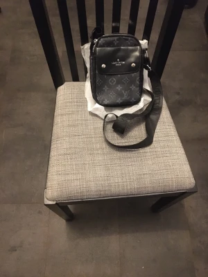 Lovis Vuisson axelremsväska läder monogram. - Lovis Vuisson axelremsväska i läder med mörkt monogrammönster och justerbart band. Har dragkedja upptill, framficka med lock och tryckknappar samt innerfack. Vid frågor eller fler bilder släng iväg ett meddelande.