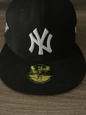 New Era Yankees svart keps 59FIFTY - Snygg svart New Era 59FIFTY keps med New York Yankees-logga i vitt framtill och broderad World Series 2000-detalj på sidan. Klassisk flat brim och strukturerad passform. Perfekt för dig som gillar streetwear och sportig stil.