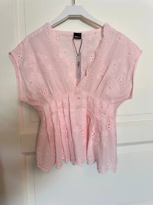 Ljusrosa broderad blus från Gina Tricot - Helt ny söt ljusrosa blus från Gina Tricot med broderade blommor och v-ringning. Blusen har korta ärmar, volangkant nertill och fina veck framtill. Perfekt för vår och sommar när du vill ha en romantisk look. Hör av er vid frågor och kom gärna med prisförslag!💞Deras nya broderie anglaise blouse🥰