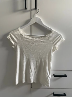 Vit spets topp  - Söt vit topp från 157 i storlek XS med spetsdetaljer runt halsringningen och ärmsluten. Kortärmad och i mjukt bomullsmaterial, perfekt för en enkel och fräsch look. Passar dig som gillar minimalistisk stil med en feminin touch.