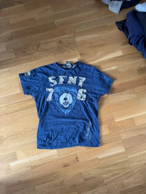 Blå Superfly t-shirt med tryck 2000 stil - Snygg blå t-shirt från Superfly med stort SFNY-tryck och siffror framtill. T-shirten har korta ärmar och coola slitna detaljer på bokstäverna. Perfekt för dig som gillar streetwear och vill sticka ut lite extra. Väldigt i stil nu