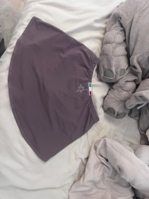 Lila karismakjol med strassdetaljer - Kort lila karisma kjol i stretchigt material med bred resår i midjan. Framtill finns en liten broderad logga och baktill en dekorativ strassdetalj. Perfekt för träning,konståkning, dans eller gymnastik.