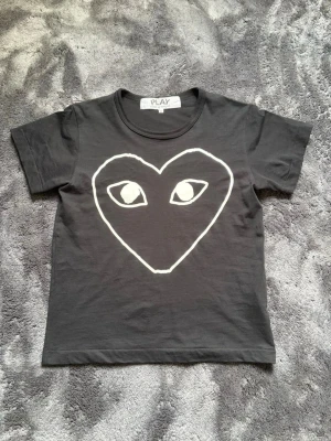Svart Comme des Garçons PLAY t-shirt - Cool svart t-shirt från Comme des Garçons PLAY med det ikoniska hjärtmotivet med ögon i vitt på bröstet. Klassisk rund hals och korta ärmar. Tillverkad i mjuk bomull som känns skön mot huden. Perfekt för dig som gillar streetwear och vill sticka ut.