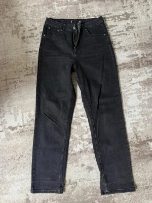 Svarta raka jeans med hög midja - Säljer ett par svarta jeans med rak passform och hög midja. Klassisk femficksmodell med dragkedja och knapp framtill. Jeansen har en enkel och stilren look, perfekta till en avslappnad outfit. Materialet är denim med lätt stretch för extra komfort.