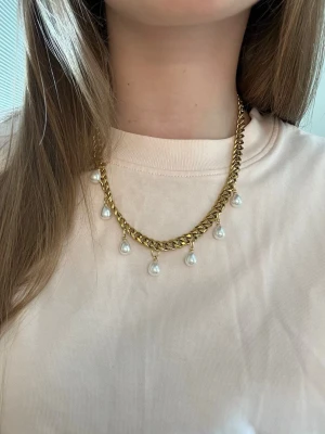 Guldhalsband med pärlhängen - Snyggt halsband i guldfärgad metall med droppformade vita pärlor som hänger längs kedjan. Kedjan har en chunky design och pärlorna ger en elegant touch. Perfekt accessoar för att lyfta din outfit. Rostfritt stål och handgjort 