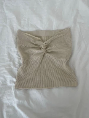 Beige ribbad bandeau tubtopp - Säljer en beige ribbad bandeau tubtopp med snygg twistdetalj framtill. Toppen är ärmlös och croppad, perfekt till jeans eller kjol. Materialet är stretchigt och mjukt, vilket gör den superbekväm att bära!!