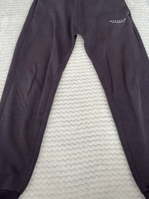 Grå mjukisbyxor från McKenzie - Säljer ett par grå mjukisbyxor från McKenzie med dragsko i midjan och ribbade muddar vid bensluten. Byxorna har en enkel design med vit logga på vänster lår. Perfekta för chill dagar eller när du vill vara bekväm.