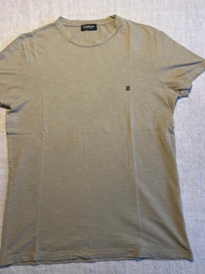 Dondup T-shirt - Stilren beige t-shirt från Dondup med rund halsringning och diskret logga på bröstet. Tillverkad i mjuk bomull och har en klassisk passform med korta ärmar. Perfekt basplagg för en enkel och clean look.