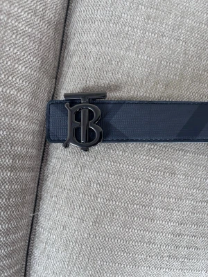 Svart Burberry bälte  - Snyggt svart bälte från Burberry med klassiskt rutmönster och ett stilrent monogramspänne i metall. Bältet är 120 cm lång och aldrig andvänt. 