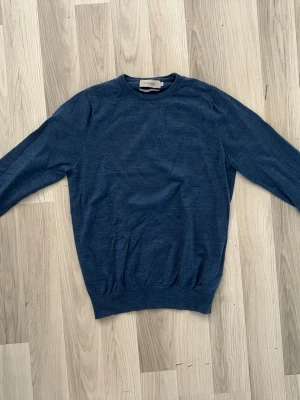 Blå merinoulltröja från Dressmann - Mörkblå stickad tröja från Dressmann Premium Collection i 100% merinoull. Klassisk rund halsringning och ribbade muddar vid ärmslut och nederkant. Perfekt för lager på lager och riktigt skön mot huden.