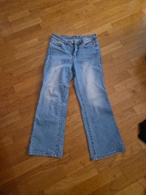 Ljusblå bootcut jeans från kappahl - Säljer ett par ljusblå bootcut jeans från kappahl i klassisk denim. Jeansen har fem fickor, bälteshällor och dragkedjegylf. Materialet är slitstarkt bomullsdenim och passformen är rak med lätt utsvängda ben. Perfekta för en avslappnad och trendig look.