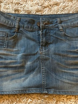 Blå jeanskjol med fickor - Säljer en klassisk blå jeanskjol med normal passform. Kjolen har framfickor, bälteshällor och stängs med knapp och dragkedja. Perfekt till vardags för en avslappnad och trendig look. Vet tyvärr inte vart den är ifrån! Pris kan diskuteras!