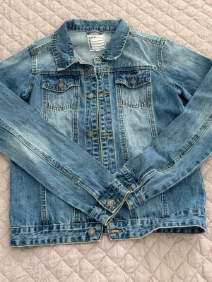 Blå jeansjacka från D.M.D - Snygg blå jeansjacka från D.M.D By denim day med klassisk tvättad look. Jackan har två bröstfickor med knappar, knappstängning framtill och en rak passform. Perfekt att slänga över en hoodie eller t-shirt för en avslappnad stil.